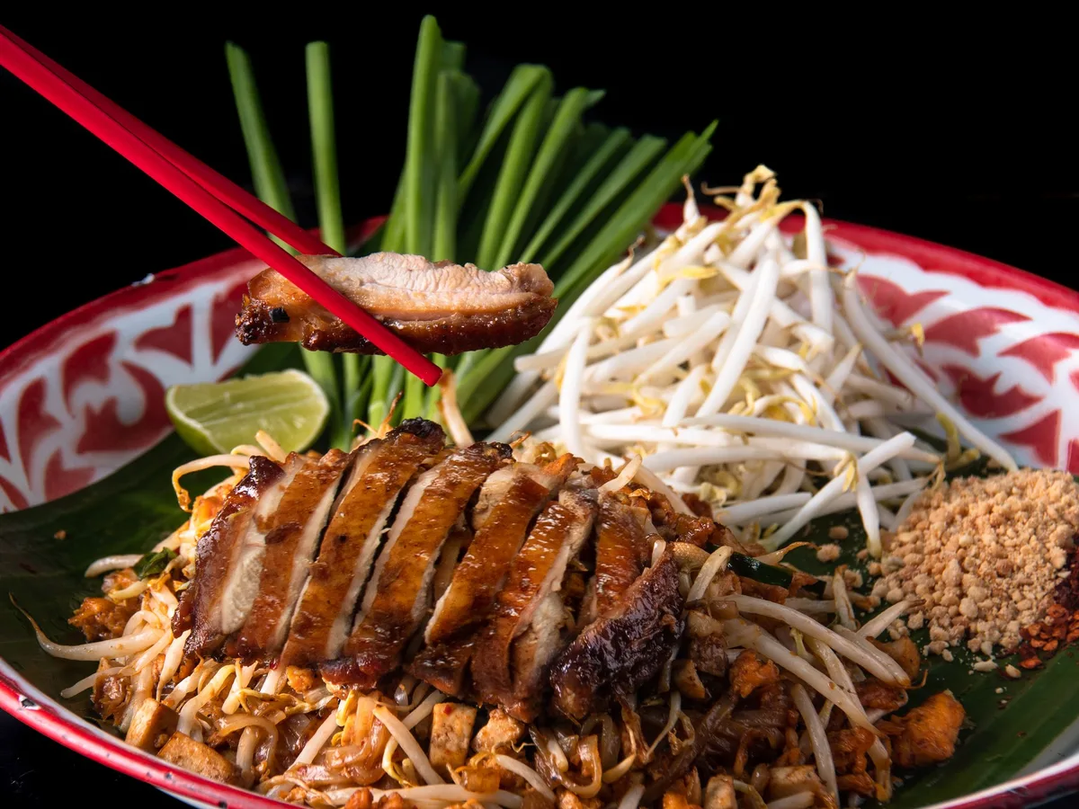 ผัดไทยท็อปไก่ย่างหั่นชิ้น เสิร์ฟพร้อมถั่วงอกและกุยช่าย