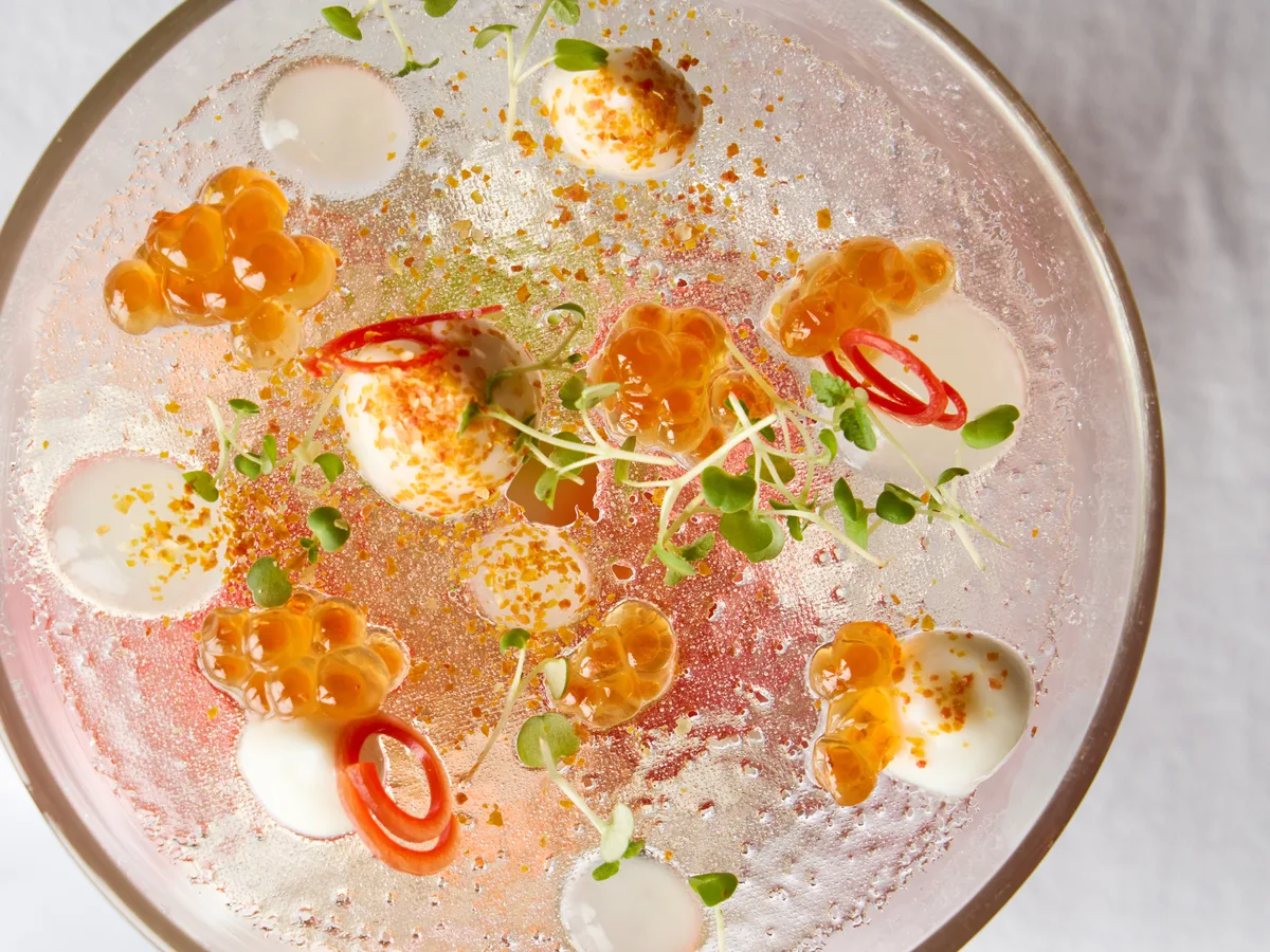อาหารคอร์สเย็นในชามแก้ว โรยไข่ปลา ดอกไม้ และพริกแดงบนซอสสีชมพู