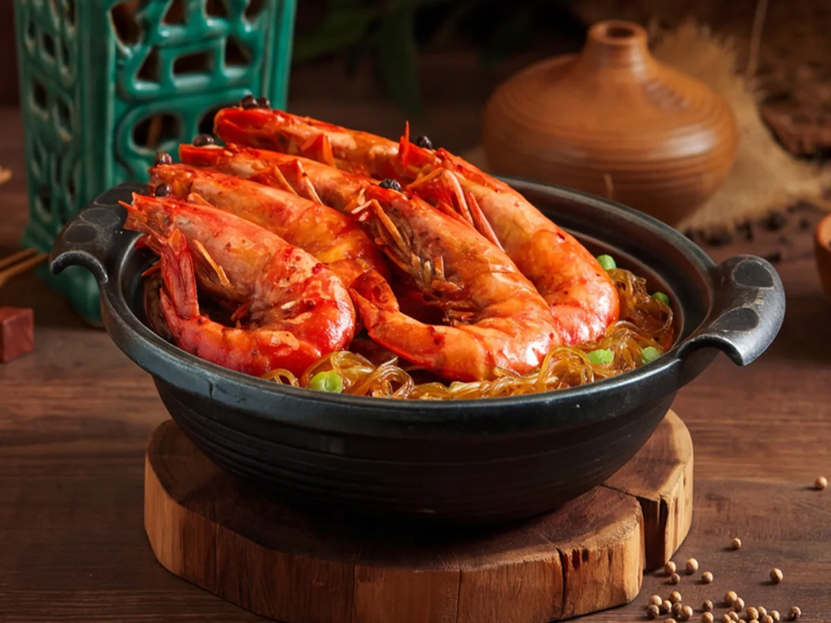 กุ้งตัวใหญ่ผัดซอสแดงในหม้อดินดำบนแท่นไม้