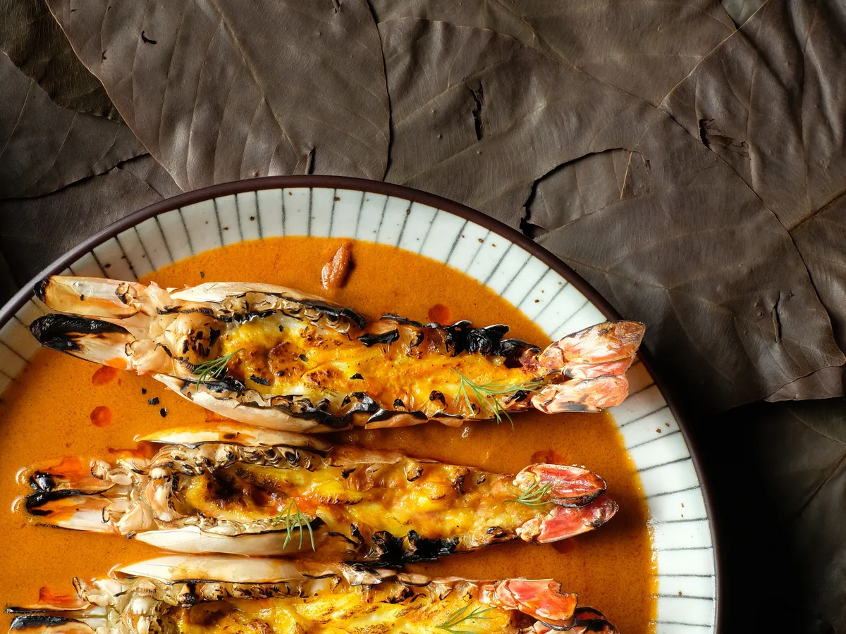 กุ้งแม่น้ำย่างในแกงสีส้มในจานกระเบื้อง