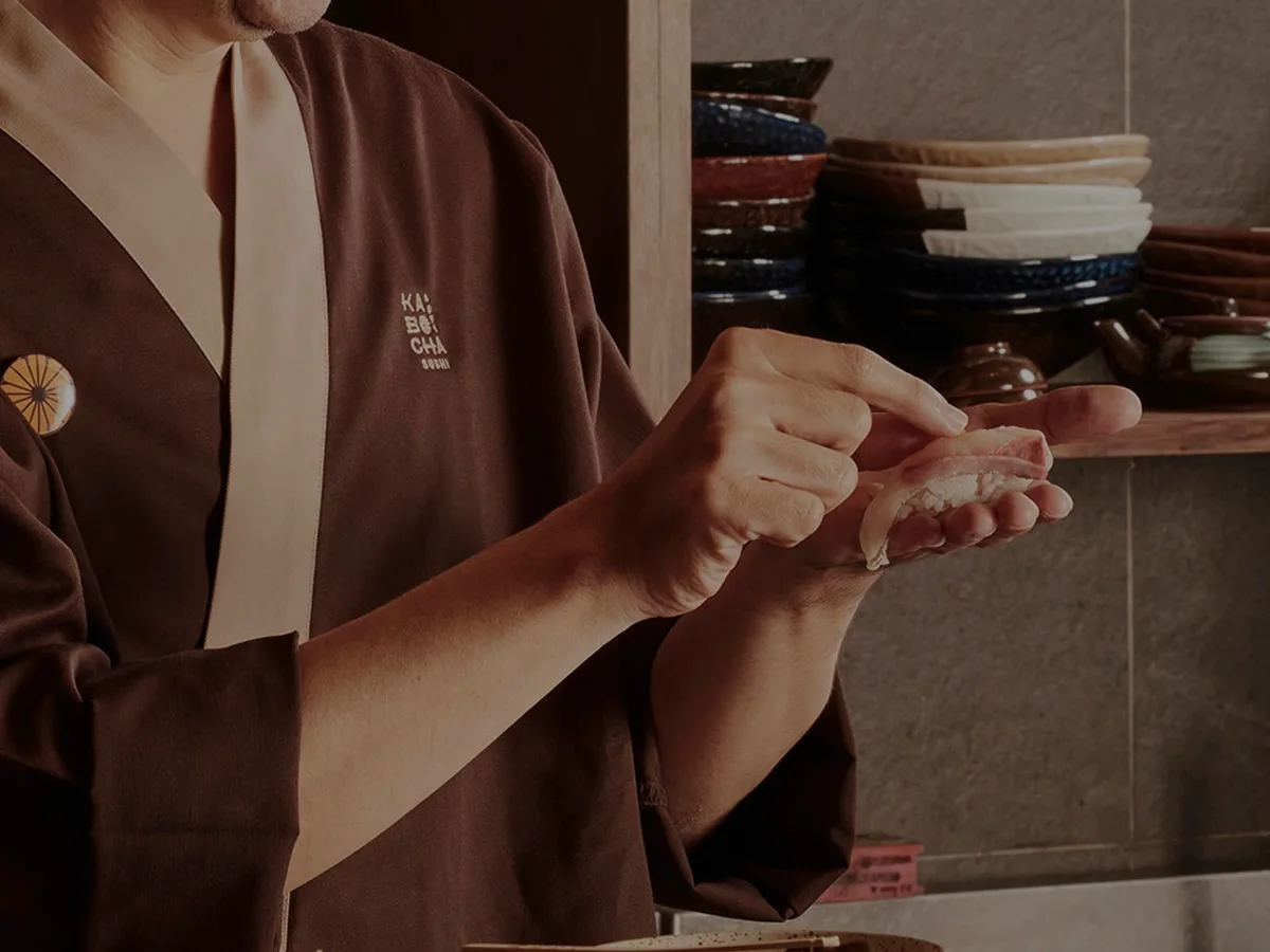 เชฟในชุดสีน้ำตาลกำลังปั้นซูชิด้วยมือ