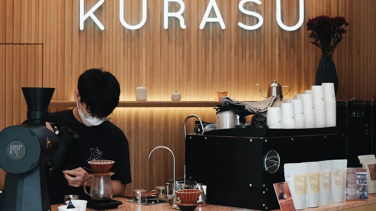 เคาน์เตอร์ไม้สีอ่อนของ Kurasu Bangkok กับบาริสต้ากำลังชงกาแฟ