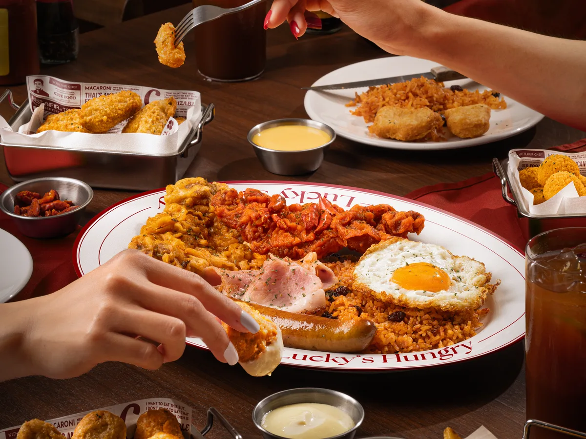 มือที่เอื้อมตักข้าวผัดอเมริกันกับไก่ทอด ไข่ดาว และมันฝรั่งทอดบนโต๊ะ