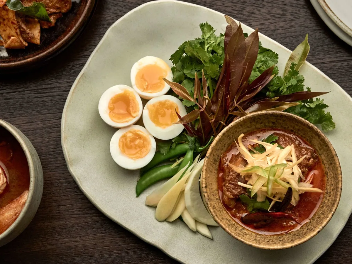 แกงในถ้วยเซรามิกกับไข่ต้มผ่าซีกและผักสดบนจานใหญ่