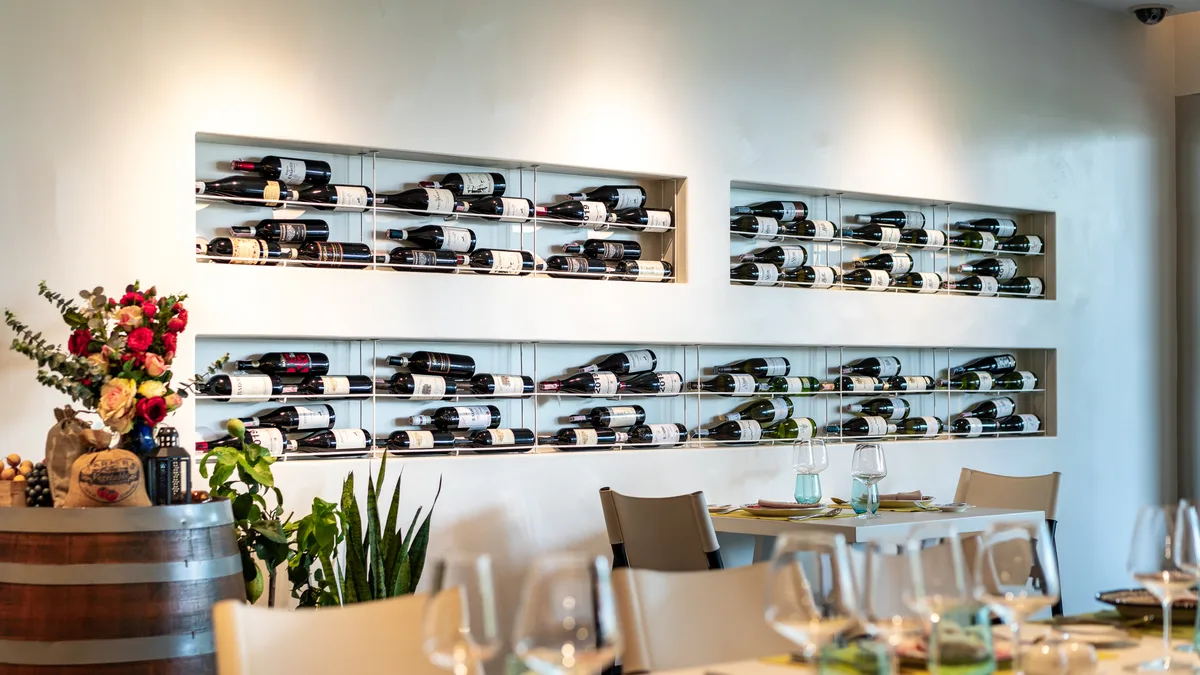ห้องอาหารสีขาวของ Otto Italian Restaurant ผนังชั้นไวน์ โต๊ะจัดแก้วไวน์และดอกไม้