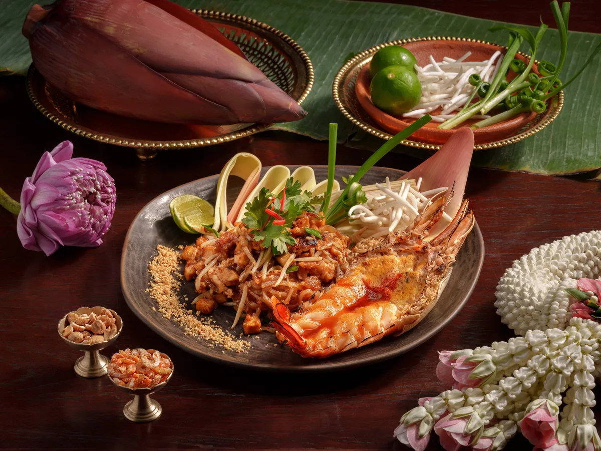 ผัดไทยกุ้งแม่น้ำบนจานกระเบื้อง แต่งด้วยพวงมาลัยมะลิ