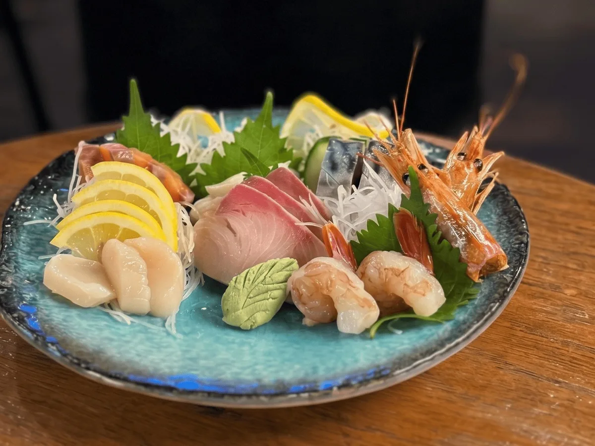 ซาชิมิรวมปลาสด หอยเชลล์ และกุ้งหวานบนจานเซรามิกสีฟ้า